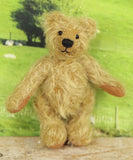 The finished Norman teddy bear standing up. Norman is a sweet gold little teddy with black eyes and a black nose.