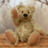 The finished Norman teddy bear sitting down and waving. Norman is a sweet gold little teddy with black eyes and a black nose.