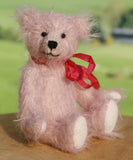 Teddy bear with a red bow sitting on a wooden surface with a blurred green background