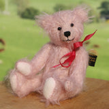 Pink teddy bear with a red ribbon on a wooden surface with a blurred green background