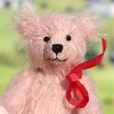 Pink teddy bear with a red ribbon against a blurred green background