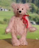 Pink teddy bear with a red bow on a wooden surface with a blurred natural background