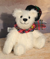 Theo sitting with his hat off to show you his face.
Theo sitting and waving. The Christmas Teddy bear sewing kit makes Theo who is a 6.5”/ 17cm (approx) fully jointed, white mohair (12mm sparse) bear wearing a black felt hat with felt holly leaves, red glass berry beads and a star sequin plus a tartan scarf with a yellow glass bead. He has black glass eyes , a cute little tail and a black embroidered nose. He is quite heavy and squidgy and very smiley.