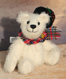 Theo sitting with his hat off to show you his face.
Theo sitting and waving. The Christmas Teddy bear sewing kit makes Theo who is a 6.5”/ 17cm (approx) fully jointed, white mohair (12mm sparse) bear wearing a black felt hat with felt holly leaves, red glass berry beads and a star sequin plus a tartan scarf with a yellow glass bead. He has black glass eyes , a cute little tail and a black embroidered nose. He is quite heavy and squidgy and very smiley.