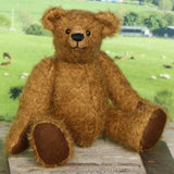 Treacle teddy bear sitting on a wooden surface with a pastoral scene in the background