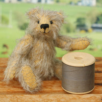 William sitting next to a reel of thread. William Miniature Mohair Teddy Bear Kit. A jointed teddy bear kit by Make A Teddy to make a 4 inch/10 cm teddy bear.